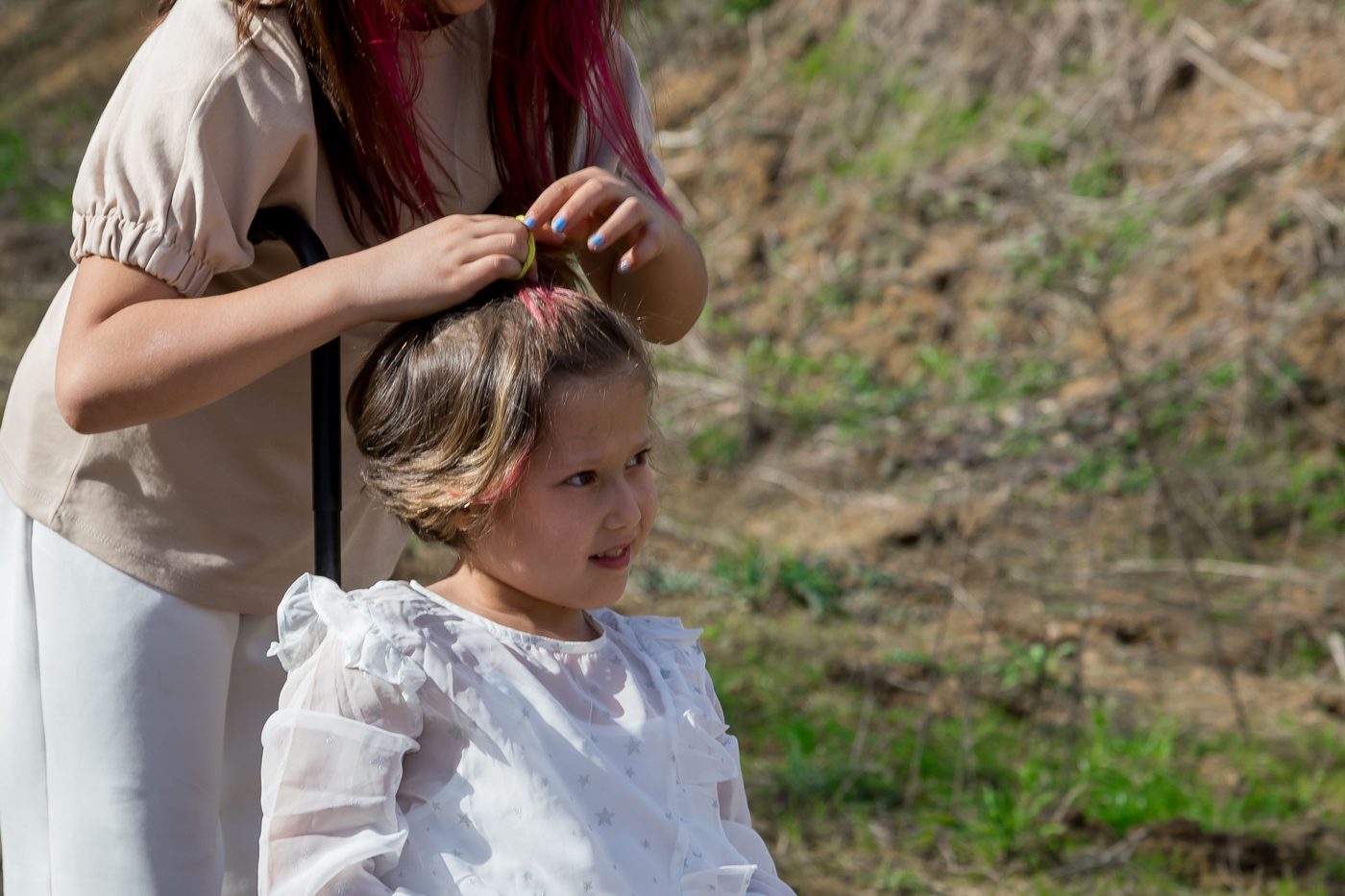 A mother brushing her daughter’s hair outdoors; the girl uses a pink wheelchair.