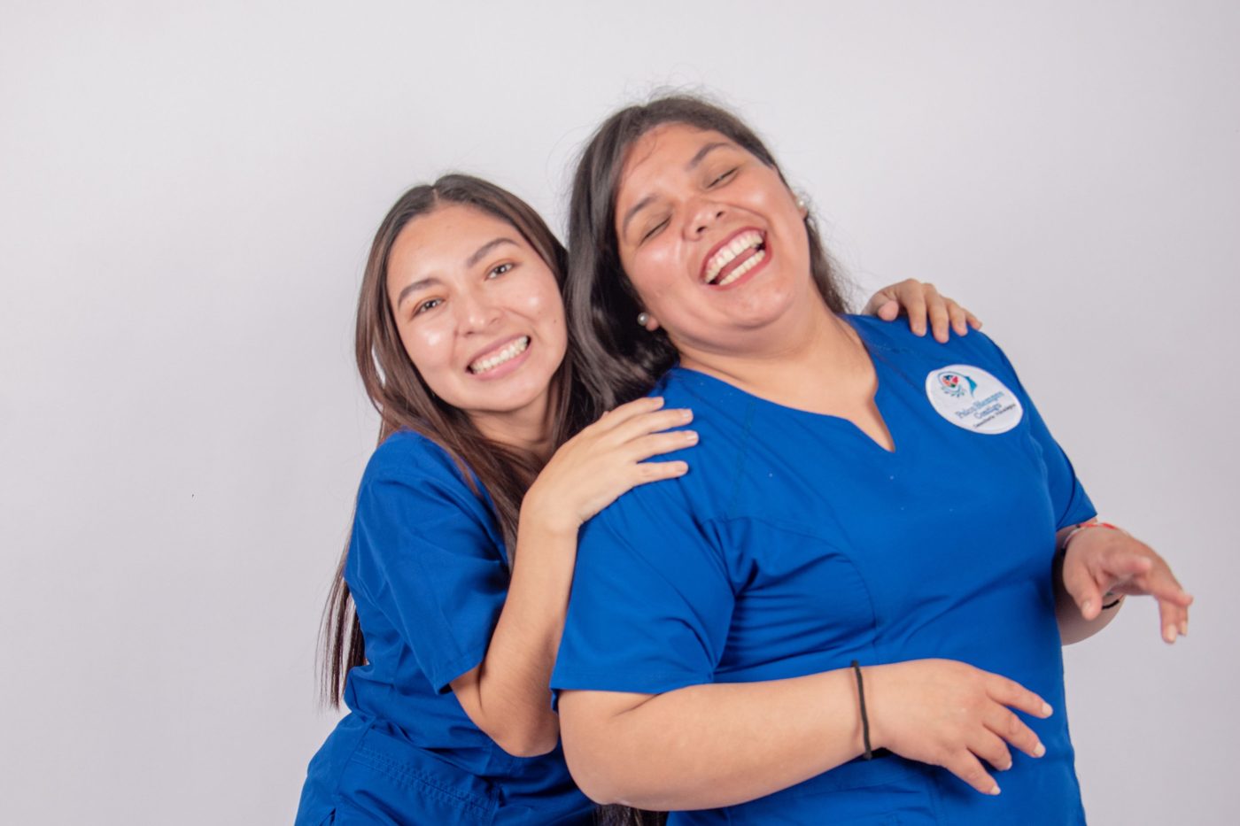 Two nurses in blue scrubs laughing together.