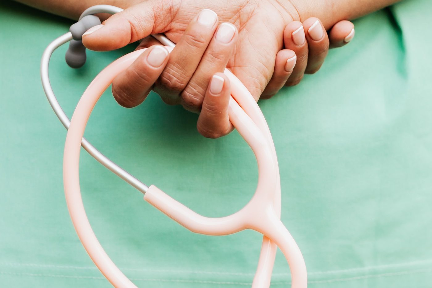 A nurse in green scrubs holding a pink stethoscope with a panda charm.