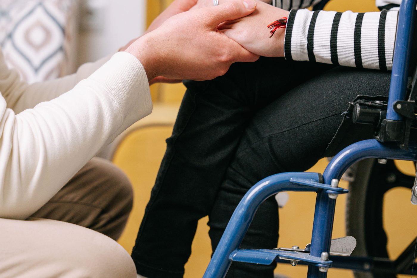 A caregiver holding the hand of a child seated in a wheelchair.