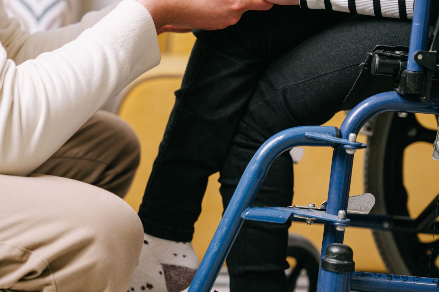 A caregiver holding the hand of a child seated in a wheelchair.